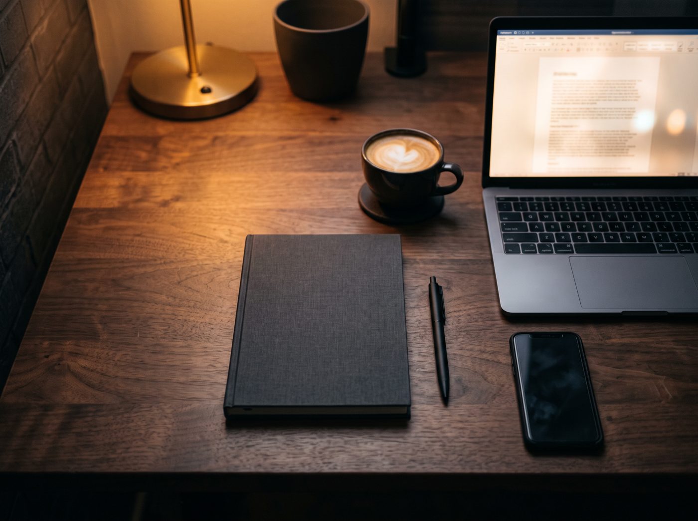 A tidy desk with a laptop, notebook and coffee in warm evening light